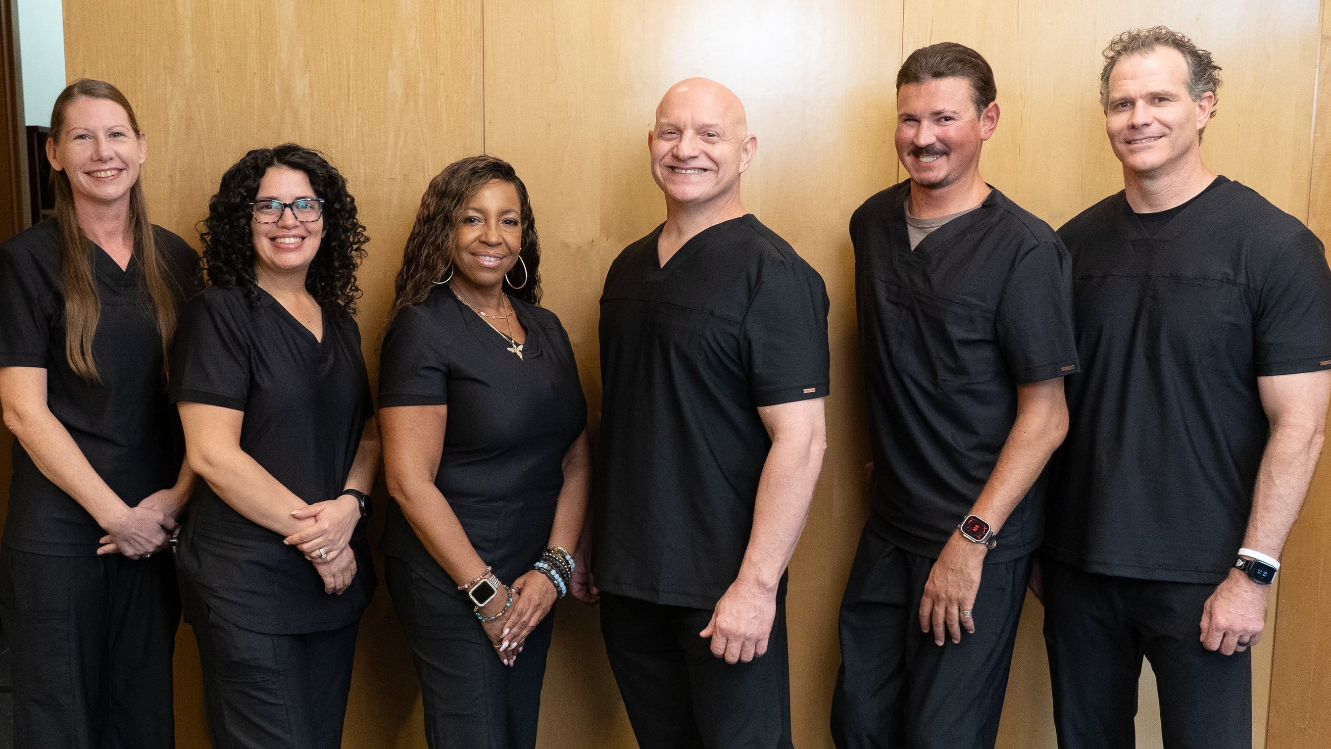 Six Causenta staff members in matching black scrubs stand together in front of a wood-paneled wall with the blue and purple Causenta logo.