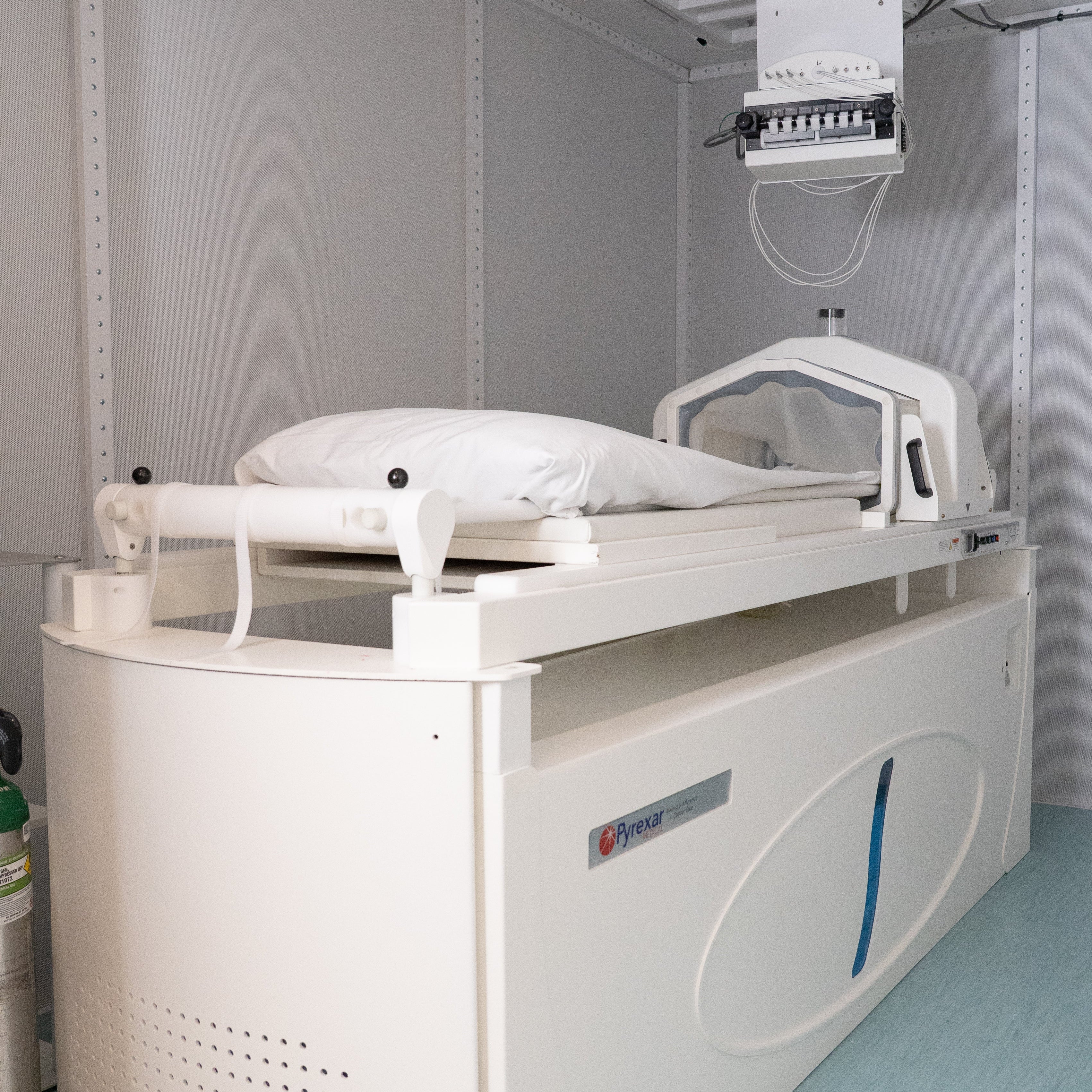Hyperthermia bed with an adjustable frame, shown inside a light gray utility room with a light blue floor.