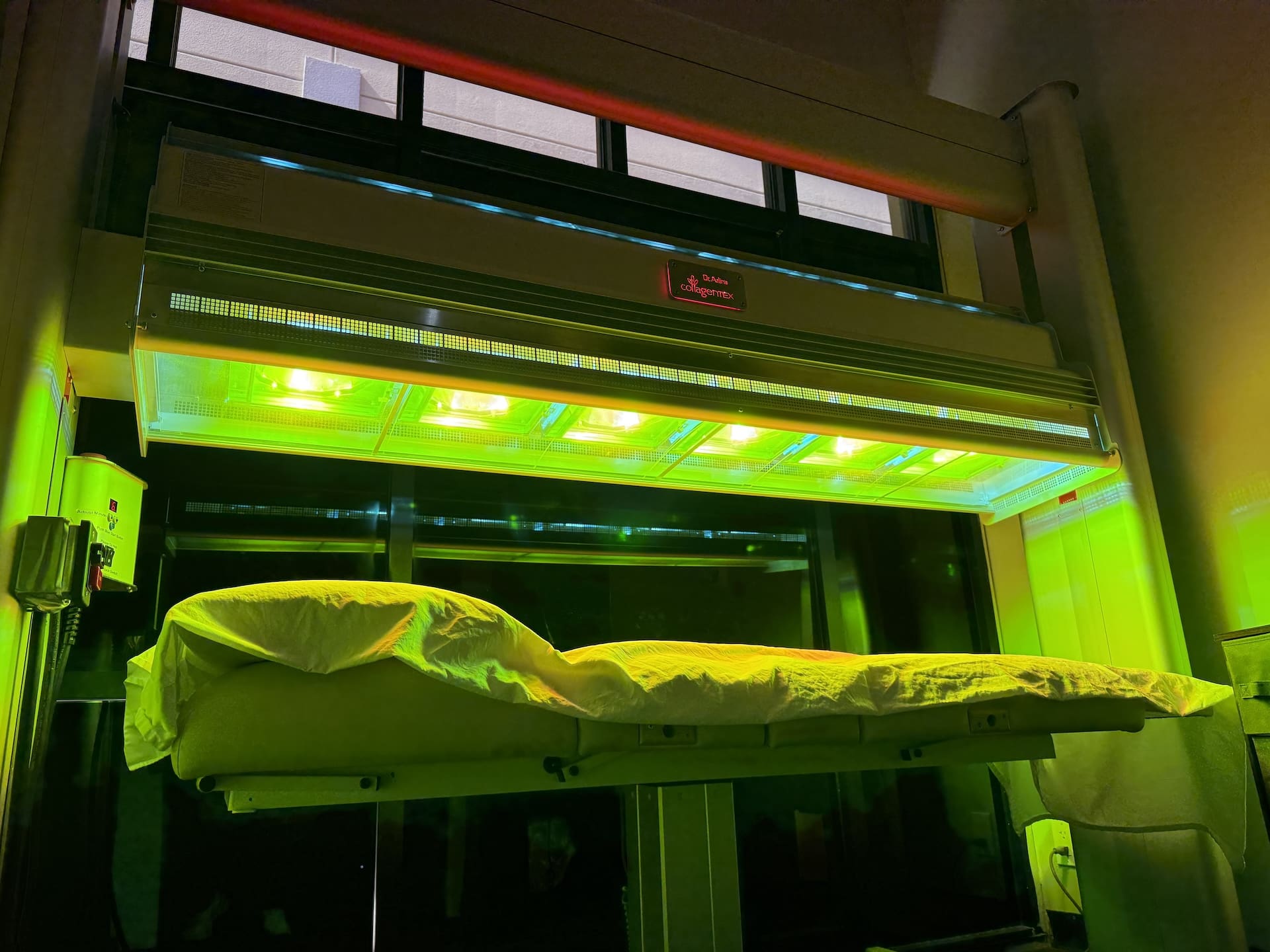 A UV light therapy panel with a bright green illuminated treatment bed, shown in a clinical or treatment room setting.
